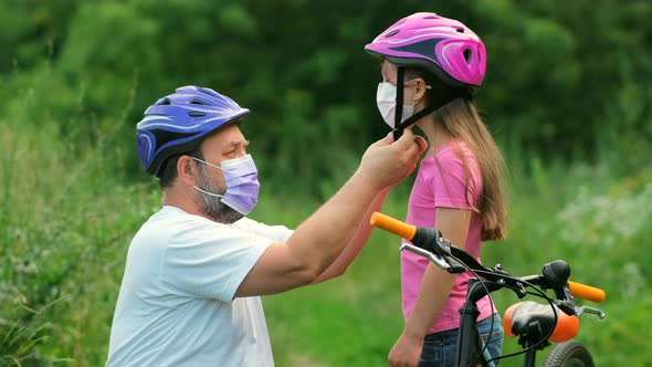 A bearded father puts on a protective Bicycle helmet for his daughter
