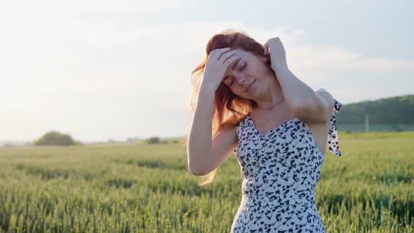 Cheerful Smiling Ginger Woman Straightens Hair in Green Wheat Field Outdoors alt