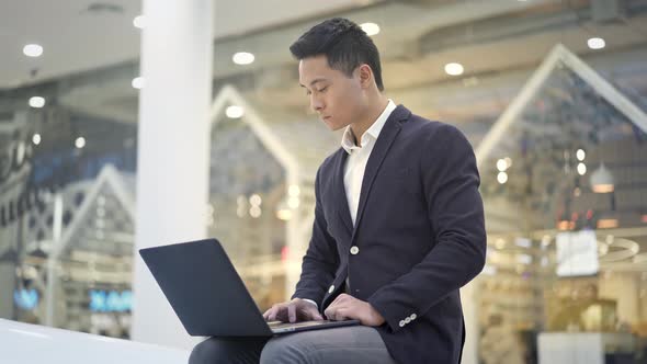 Middle Shot of Asian Male Businessman in Suit Working with Laptop on His Knees