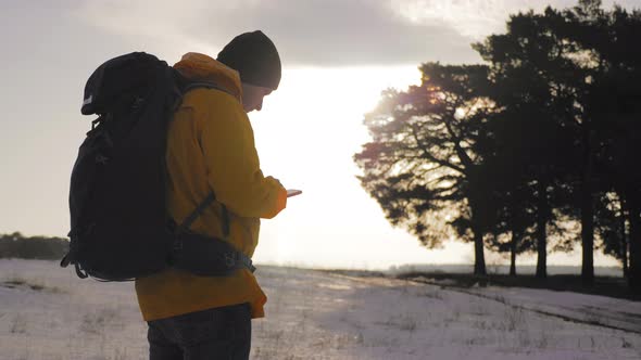 Man Hiker Backpacker Traveler Camper with Her Phone Looks at a Map or Route Under Sun Light alt
