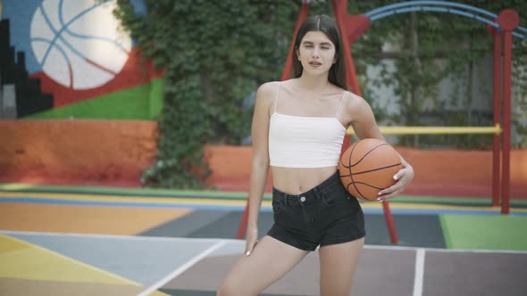 Charming Brunette Sportswoman Posing with Orange Basketball Ball on Outdoor Court alt