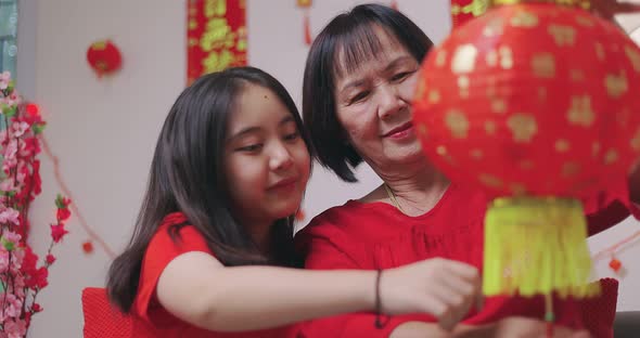 Asian Senior Woman And Niece Decorate House For Chinese New Year Celebrations With Flowers. alt