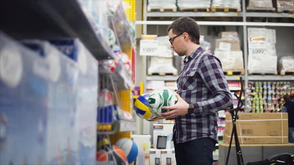 A Man Looks at Volleyball and Soccer Balls in a Hypermarket for a Sports Game alt