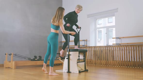 Mature Female Doing Exercises on Pilates Chair During Workout in Gym with Help of Coach