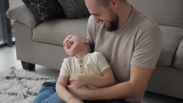 Happy loving young adult dad having fun tickling cute preschool kid son relaxing together, cheerful alt