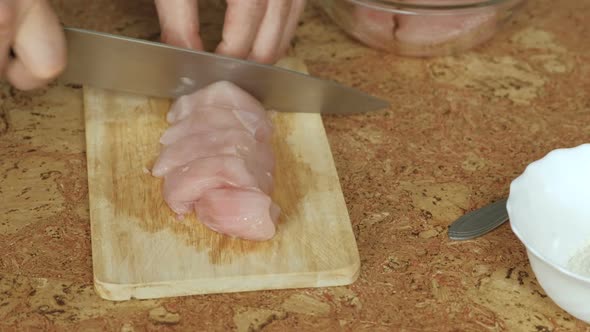  Man's Hands Cutting a Chicken Meat on a Wood Board on the Table.