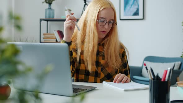 Annoyed Child Studying Online with Laptop Typing and Taking Notes at Desk in Living Room alt