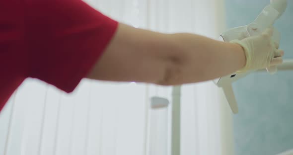 Dentist Lowers the Lamp to the Desired Position and Turns It on alt