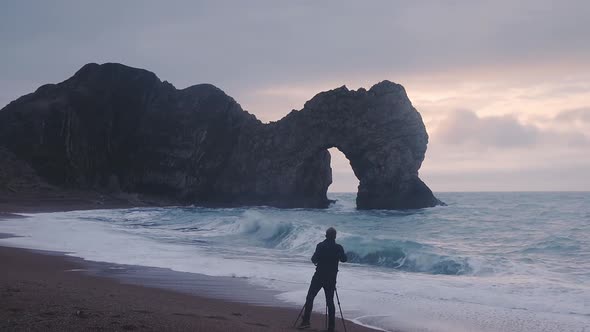 A Male Photographer With Camera On A Tripod Taking Photo Of The Natural Limestone Arch Durdle Door O alt