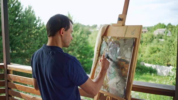 A Male Artist Paints a Picture with a Brush in Nature alt