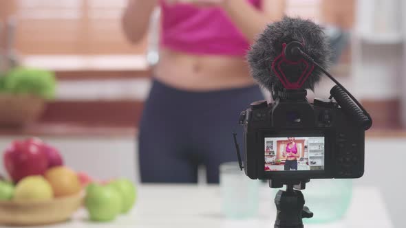 Young female using camera recording when she eating fruits in the kitchen.