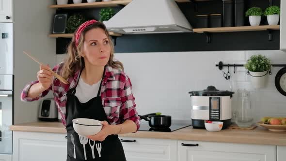 Carefree happy young woman housewife dancing alone cooking meal