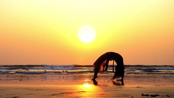 Silhouette of Young Woman Doing Gymnastic Bridge on the Beach 