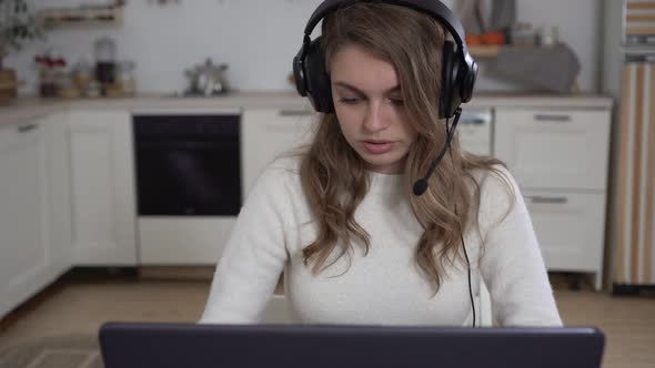 Young Woman at Home with a Laptop in Headphones with a Microphone alt