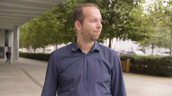 A Caucasian Man Applauds to the Camera with a Smile By an Office Building in an Urban Area