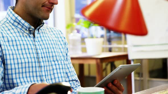 Male business executive having coffee while using digital tablet alt