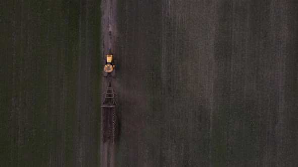 Aerial view of a modern yellow tractor rides across the field alt