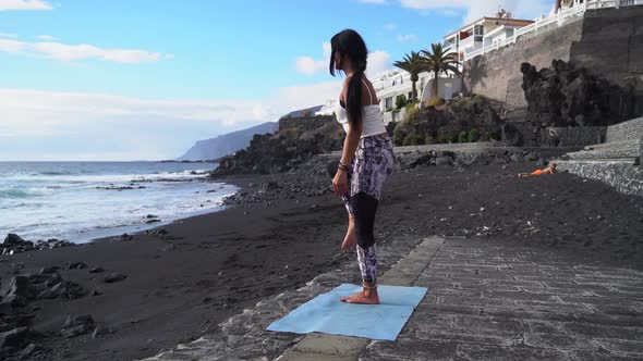 Woman in Sport Clothes Practicing Yoga and Meditating on Beach in Morning alt
