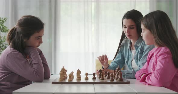 Young mother teaching chess to her daughters