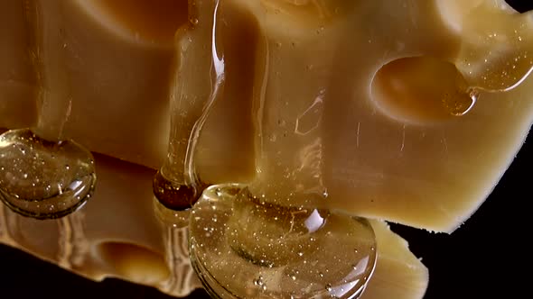 Drops of honey flow down from the cheese on a mirrored black background. alt
