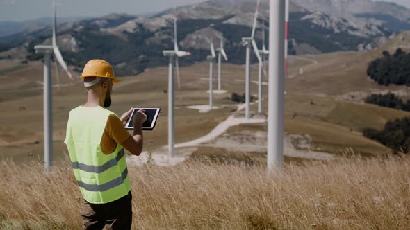 Adult engineers  in yellow hard hat and green uniform checking the wind turbine system alt