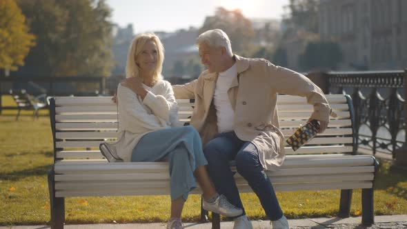 Senior Woman Is Delighted with Gift From Husband Siting Together on City Bench alt
