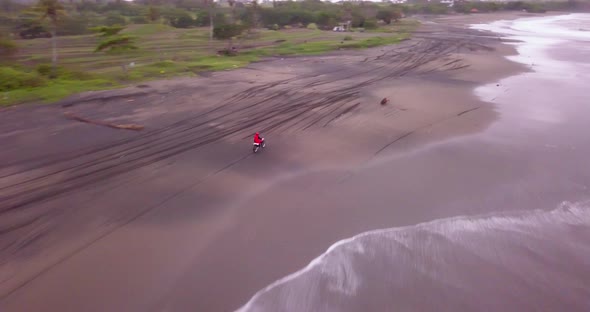 Aerial drone view of a man riding his motocross motorcycle on the beach alt