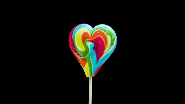 Caramel Lollipop Heart Multicolored On A Stick Spinning On A Black Background. alt