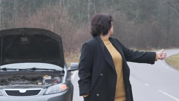 Woman at the Background of Broken Car in the Forest Trying Hitchhiking Other Cars