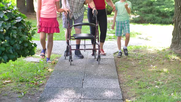 young caregiver accompanies with the grandchildren an elderly gentleman helping him to walk alt