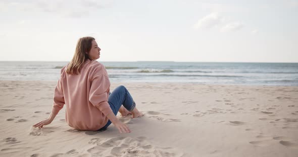 Young Hipster Woman Sitting on a Beach Looking Far Away Hugging Knees