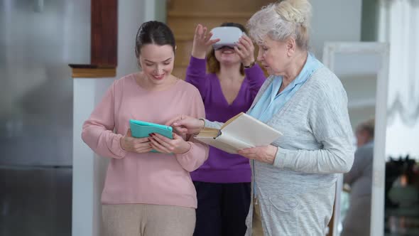 Smiling Positive Senior Grandmother with Book and Young Granddaughter with Tablet Talking As alt