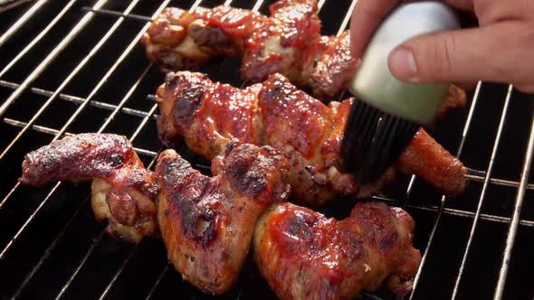 Male Hands are Smearing Delicious Chicken Wings with a Tomato Sauce on the Grill alt
