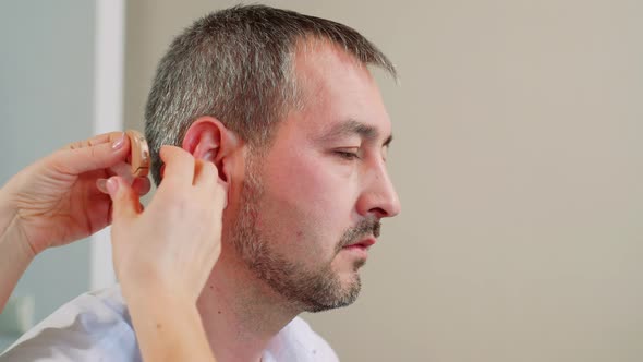 Woman Doctor Puts a Hearing Aid on A Man. alt