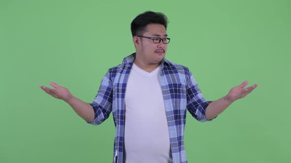 Happy Young Overweight Asian Hipster Man Comparing Something alt