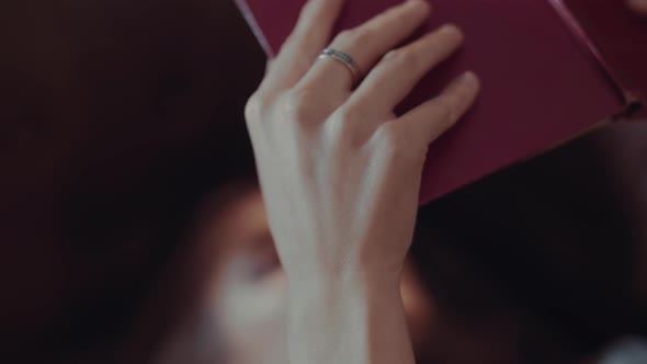 Young Attractive Caucasian Woman Holds a Book in Her Hands and Reads It While Lying on the Couch in alt