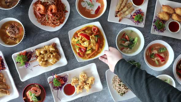 Male hand picking up thai cuisine dish from table center. alt