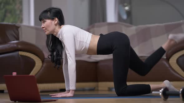 Side View Portrait Concentrated Sportswoman Raising Leg in Slow Motion in Position on All Fours alt