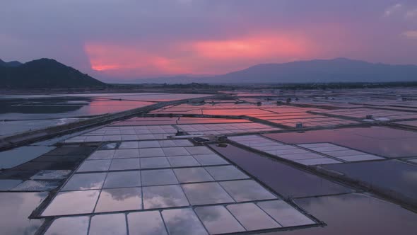 Drone flying over vast salt fields spread amidst mountains during golden hour in Phan Rang, Vietnam. alt