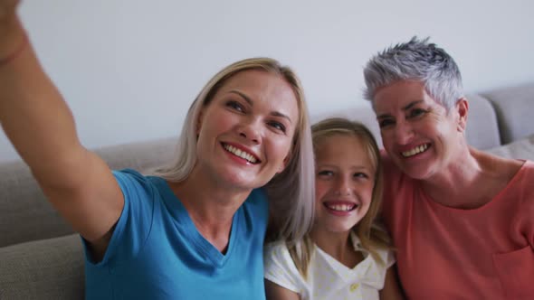 Caucasian grandmother, mother and daughter smiling while taking a selfie with smartphone at home alt
