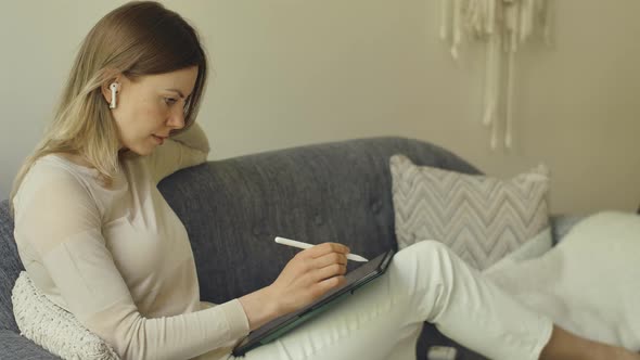 Woman with Tablet Using Pencil Tapping and Painting at Home on Sofa