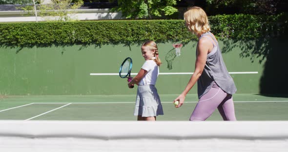 Caucasian mother teaching her daughter to play tennis at tennis court on a bright sunny day alt