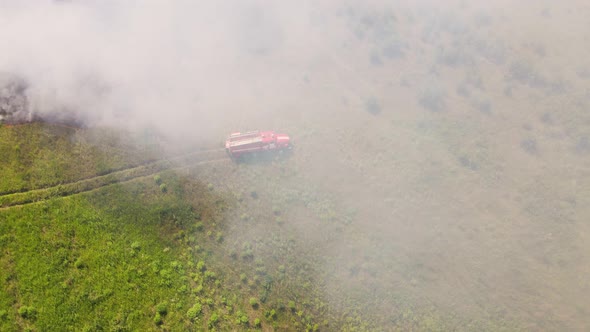 A Fire Engine is Standing in the Field Shrouded in Smoke From the Fire alt