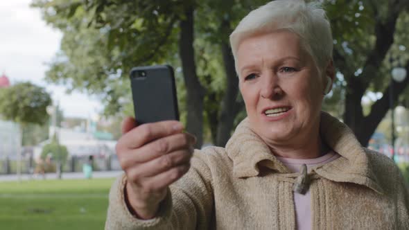 Confident Senior Caucasian Woman Grandma with Modern Wireless Headphones Making Video Call Looking alt