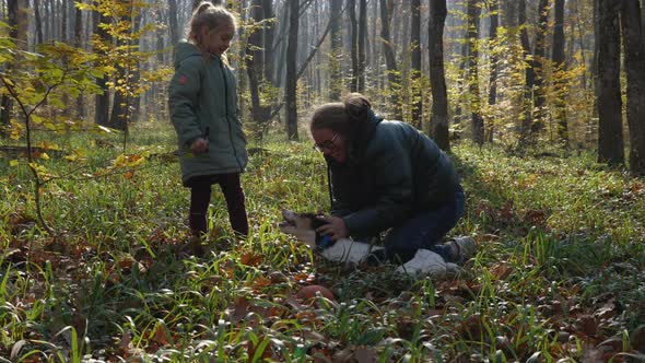 Happy mother and daughter playing with the dog in the autumn forest alt