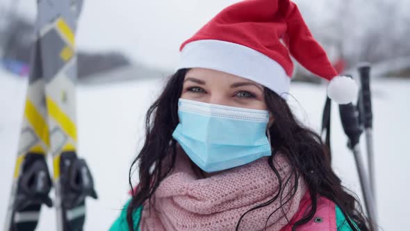 Headshot of Joyful Smiling Young Woman in Covid Face Mask and Christmas Hat Looking at Camera alt