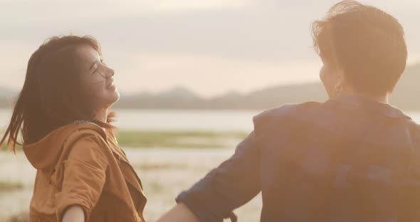 Young asia campers couple standing raised arms at campsite near beach nd fun when sunset in evening.