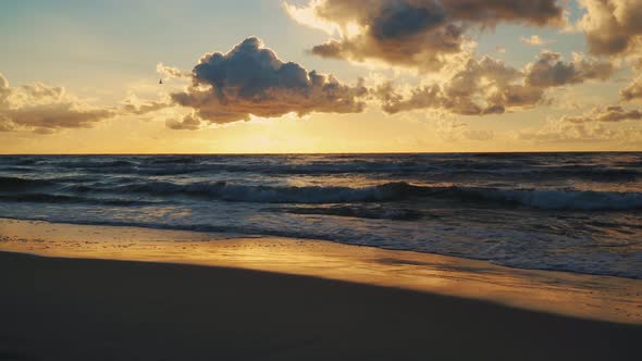 Sunset Behind Clouds Over Sea Waves and Sandy Beach alt
