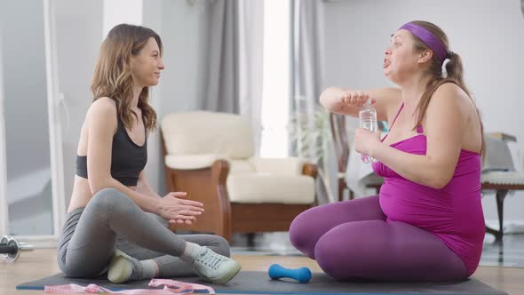 Side View Portrait of Smiling Positive Beautiful Slim Woman Giving Refreshing Water to Excited Obese alt