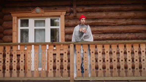 Woman in a Knitted Red Hat and Scarf Drinks Hot Tea Standing